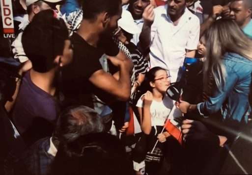 Young girl in wheel chair speaks to cameras as crowd gathers around her waiting for their turn to speak.